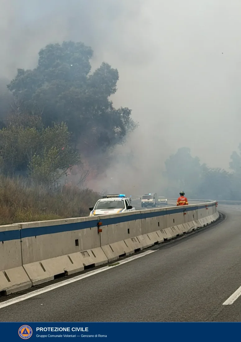 Le fiamme tra la vegetazione della scarpata a ridosso della carreggiata; oltre il new jersey un'auto della protezione civile con i lampeggianti accesi e un operatore con casco e divisa arancione