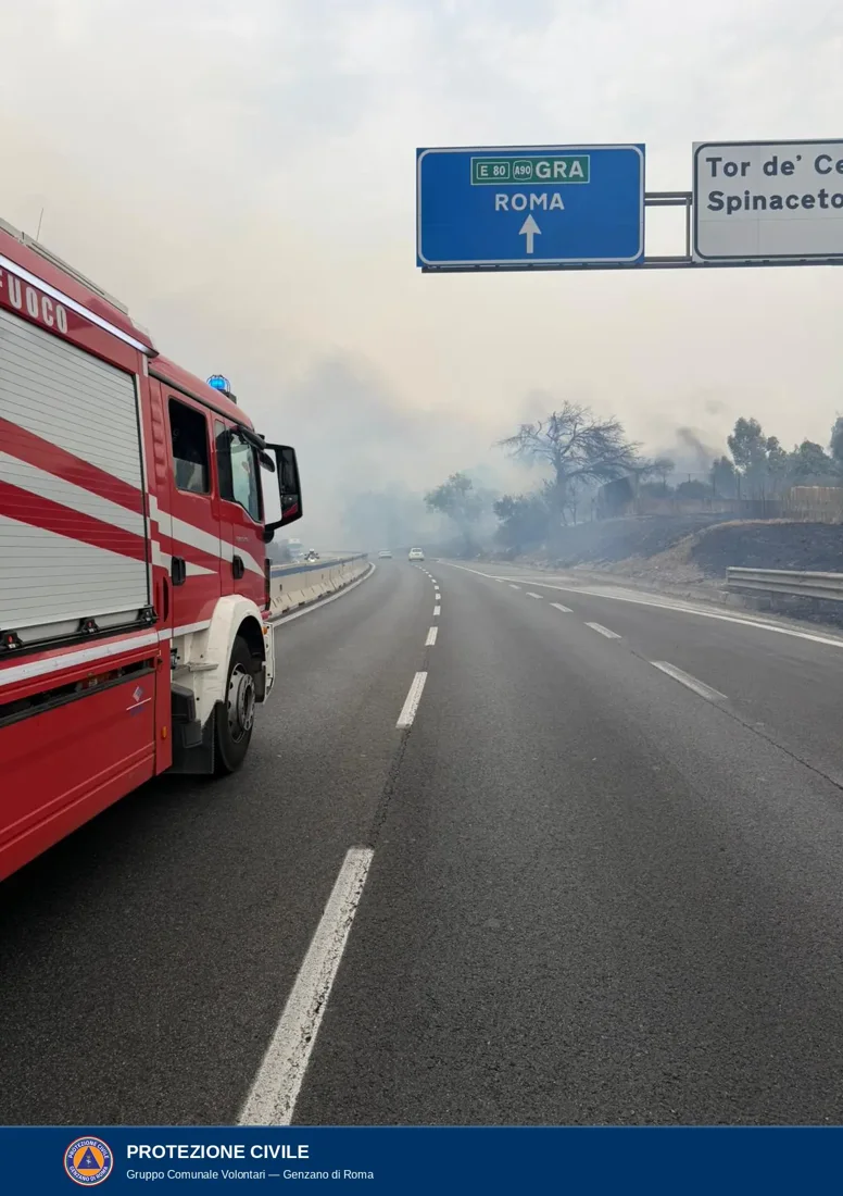 Un mezzo dei Vigili del Fuoco fermo sulla via Pontina sotto i cartelli per il Grande Raccordo Anulare, Tor de' Cenci e Spinaceto; il fumo attraversa la carreggiata e la scarpata a destra è annerita